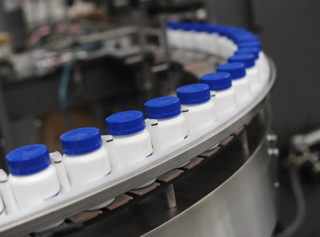 Blue Capped Drug Bottles on Conveyor s part of an automated packaging supply chain system, set in an industrial manufacturing environment.