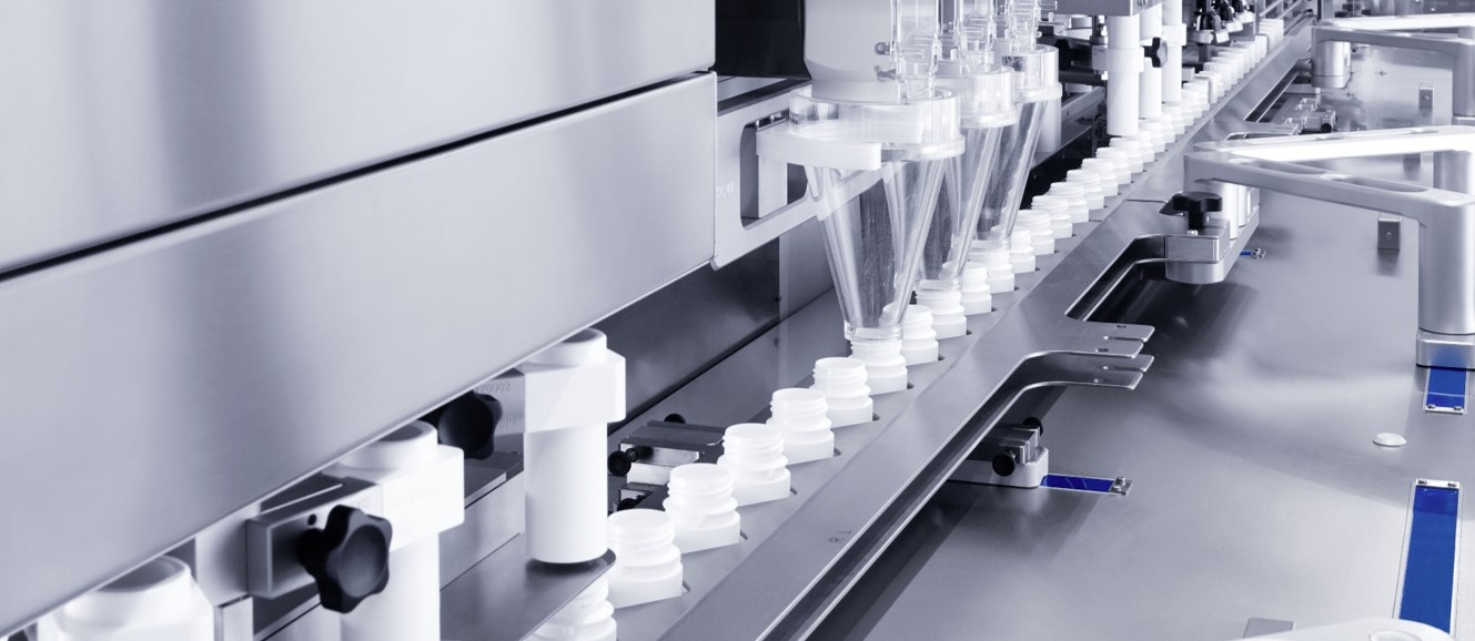 Close-up of the Uhlmann bottling line with multiple dispensing units filling clear funnels with blue capsule medications, indicating high precision in medication packaging processes.