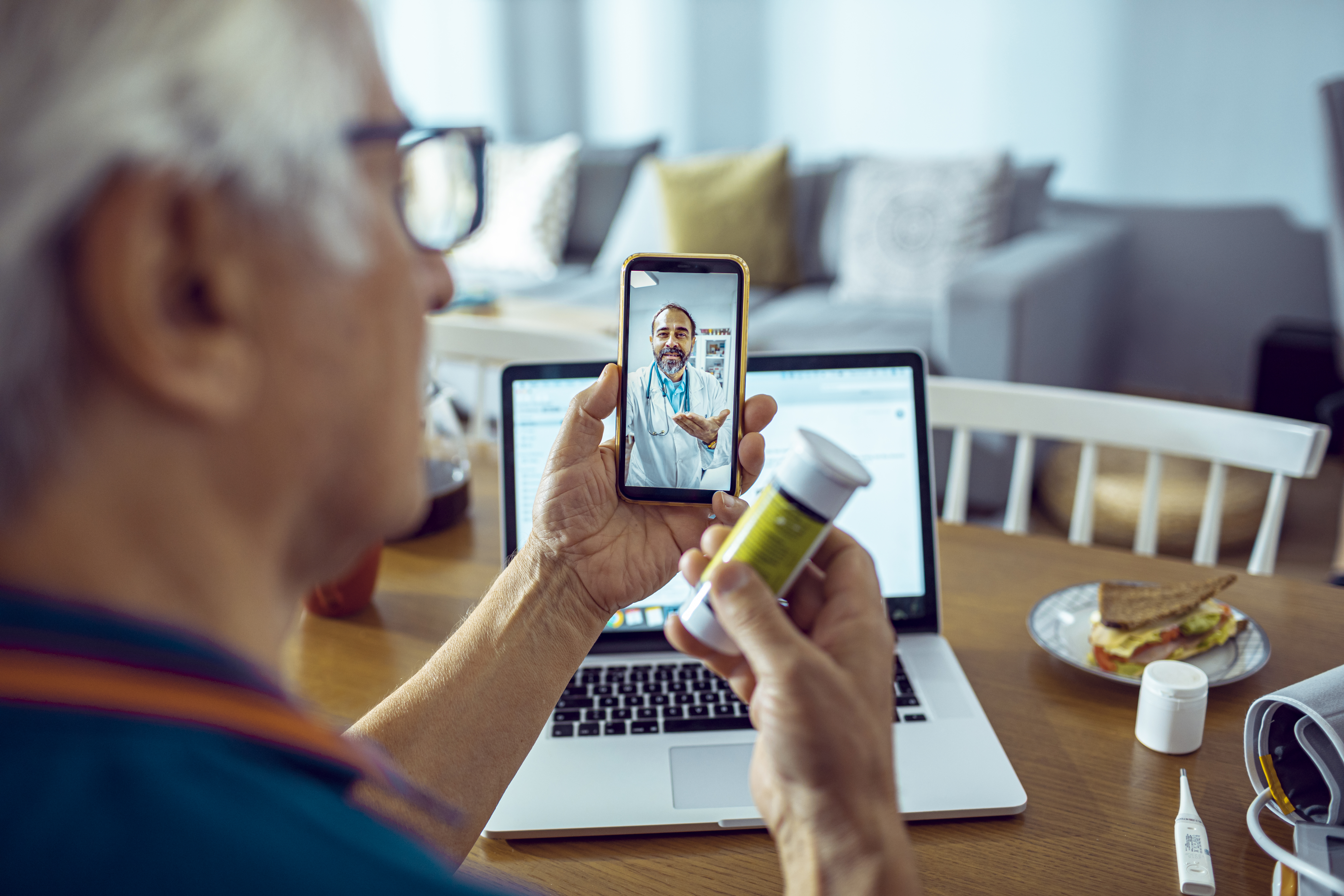 An elderly man holding a medication bottle, which features smart packaging, engages in a video consultation with a doctor via his smartphone.